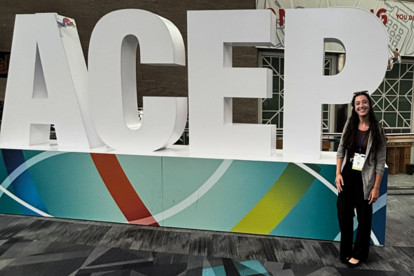 Larissa Dean standing in front of a large ACEP floor sign.